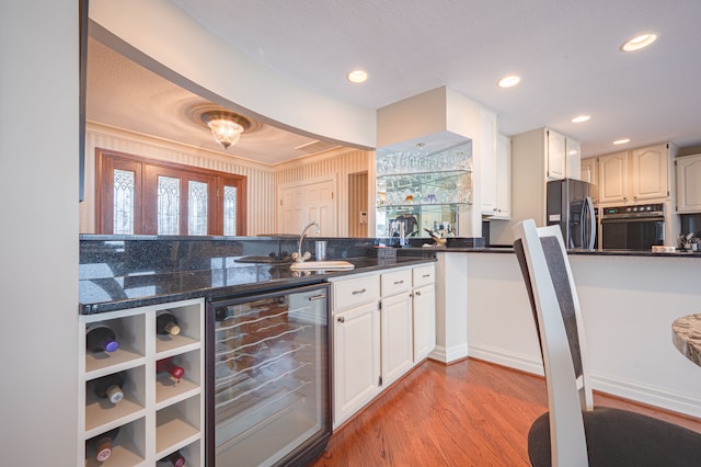 kitchen featuring wine cooler, recessed lighting, black oven, light wood finished floors, and stainless steel fridge