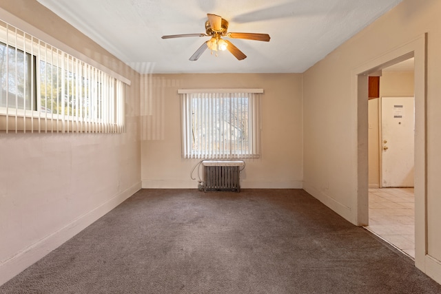 carpeted empty room featuring tile patterned floors, radiator, a ceiling fan, and baseboards