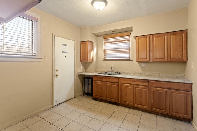 kitchen featuring baseboards, light countertops, light tile patterned floors, brown cabinetry, and a sink