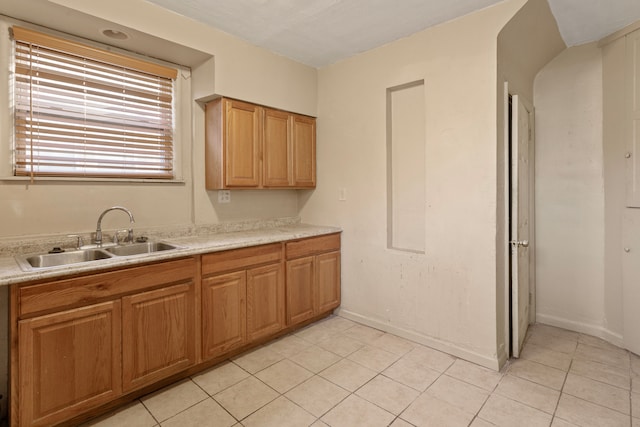 kitchen featuring a sink, baseboards, light tile patterned flooring, and light countertops