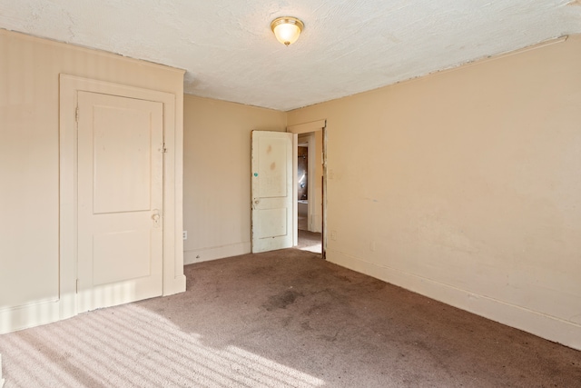 carpeted empty room with a textured ceiling and baseboards