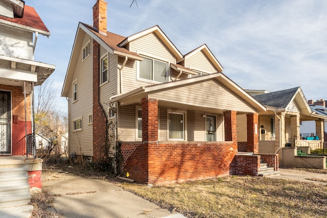 view of front facade with brick siding, covered porch, and a chimney