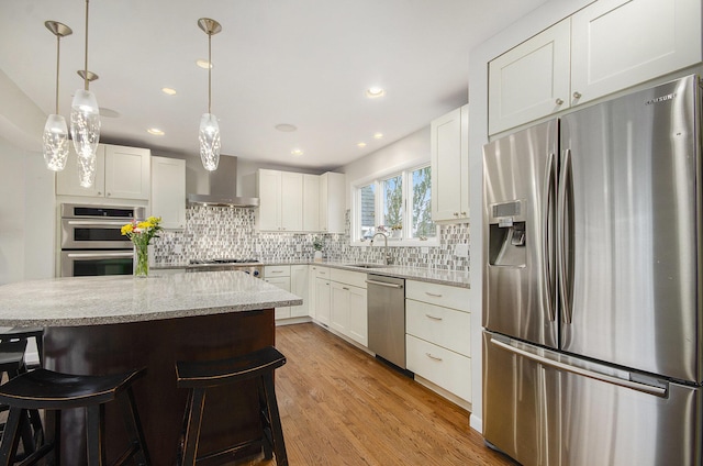 kitchen with a breakfast bar area, stainless steel appliances, tasteful backsplash, light wood-style floors, and wall chimney exhaust hood