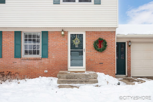 snow covered property entrance featuring a garage and brick siding