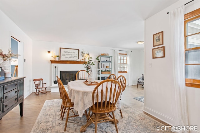 dining space with light wood-type flooring, baseboards, and a glass covered fireplace