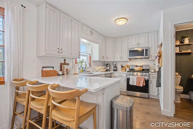 kitchen with appliances with stainless steel finishes, white cabinets, light wood-type flooring, a peninsula, and a kitchen breakfast bar