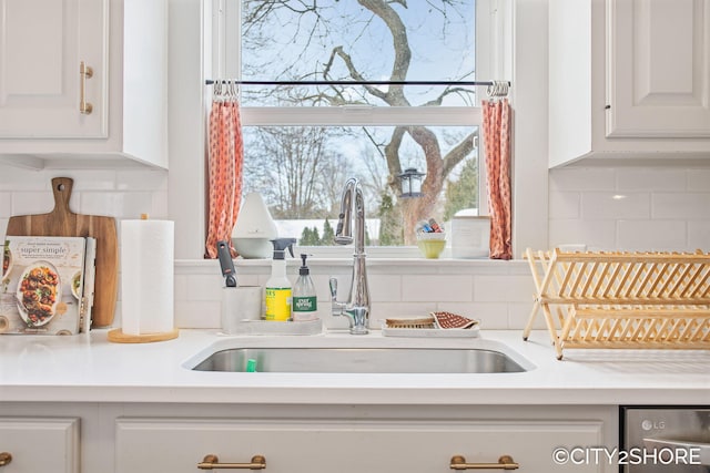 kitchen featuring decorative backsplash, white cabinetry, light countertops, and a sink