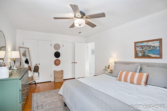 bedroom with ceiling fan, wood finished floors, and two closets