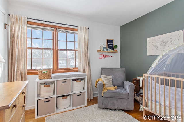 bedroom with a nursery area, baseboards, and wood finished floors