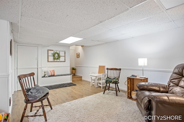 living area featuring a wainscoted wall, a drop ceiling, and wood finished floors