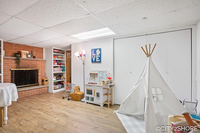 recreation room with built in shelves, a drop ceiling, a fireplace, and wood finished floors