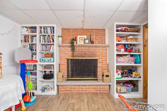 recreation room with a drop ceiling, a fireplace, wood finished floors, and built in features