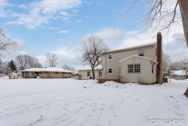 snow covered back of property with a garage and a chimney