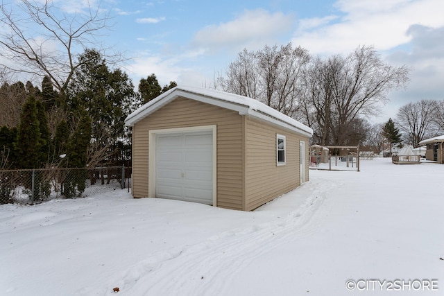 snow covered garage with a detached garage and fence