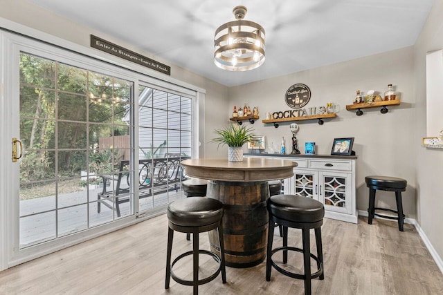 bar featuring a bar, light wood finished floors, baseboards, and an inviting chandelier