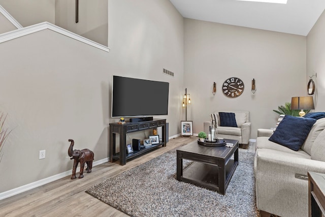 living area with a high ceiling, wood finished floors, visible vents, and baseboards