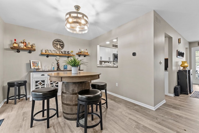 bar featuring a bar, light wood-style flooring, and baseboards