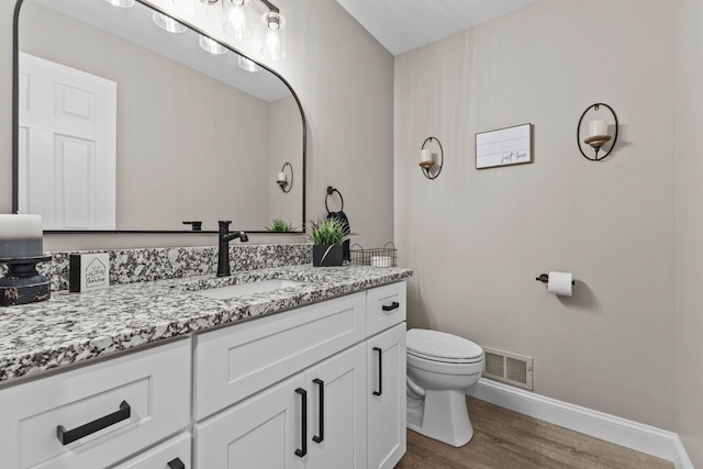 bathroom with toilet, wood finished floors, vanity, visible vents, and baseboards