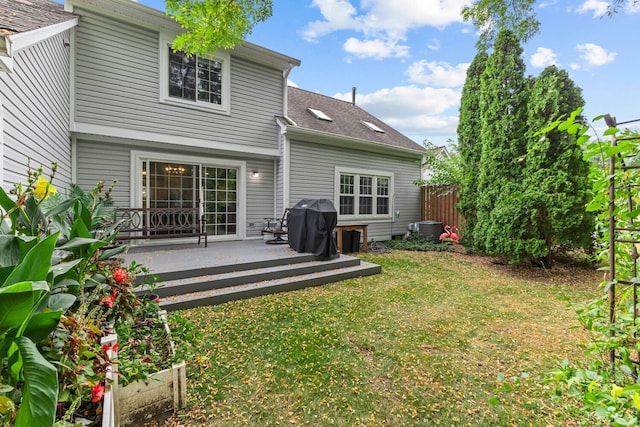 rear view of house with central air condition unit, roof with shingles, fence, and a yard