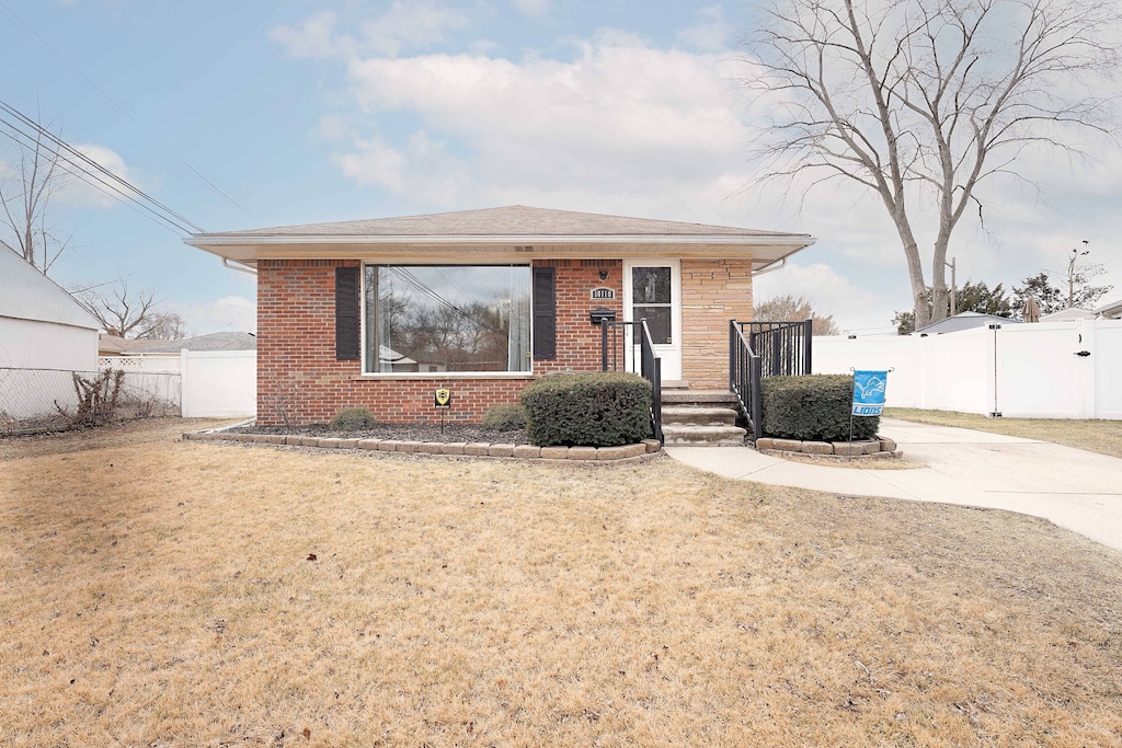 bungalow-style house featuring concrete driveway, brick siding, fence, and a front lawn