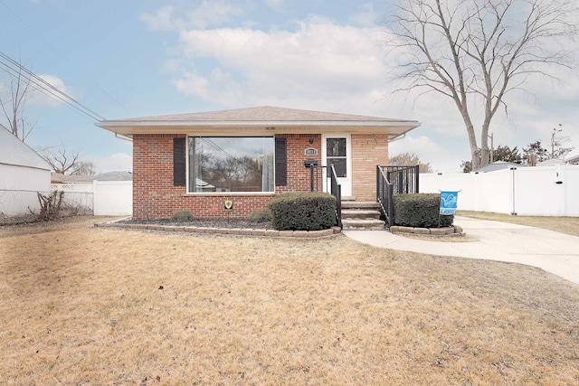 bungalow-style house featuring concrete driveway, brick siding, fence, and a front lawn