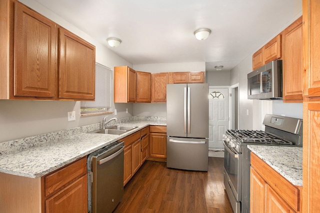 kitchen featuring dark wood-type flooring, a sink, appliances with stainless steel finishes, brown cabinetry, and light stone countertops