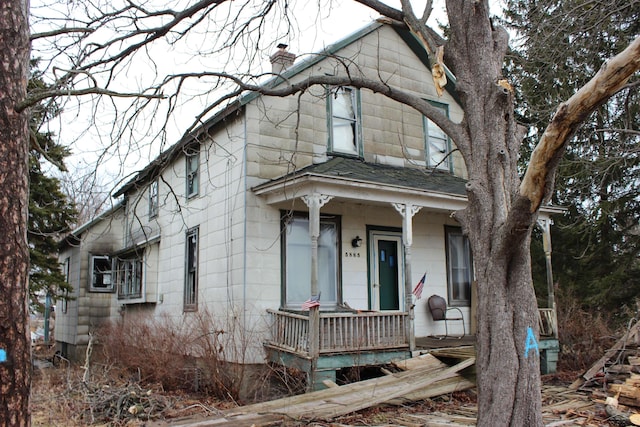 view of front facade featuring covered porch, a chimney, and roof with shingles