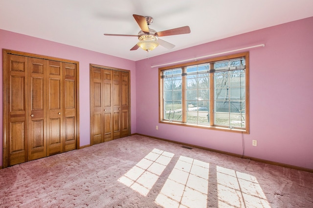 unfurnished bedroom featuring visible vents, baseboards, carpet, multiple closets, and a ceiling fan