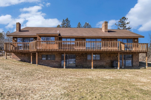 rear view of house with a deck, a lawn, brick siding, and a chimney