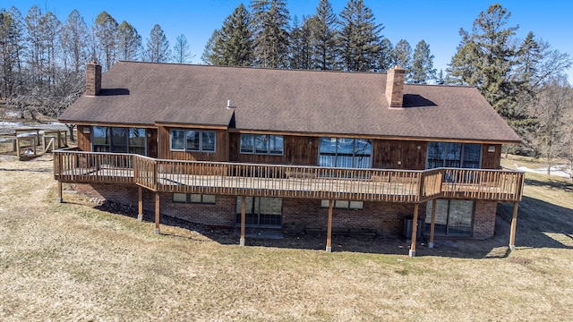 rear view of property featuring a yard, roof with shingles, a wooden deck, and a chimney