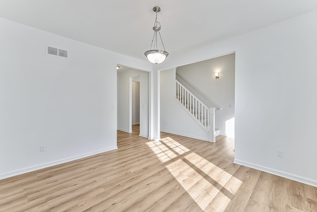 spare room with light wood-style floors, visible vents, baseboards, and stairs