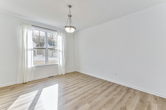 empty room featuring light wood-style floors, visible vents, and baseboards