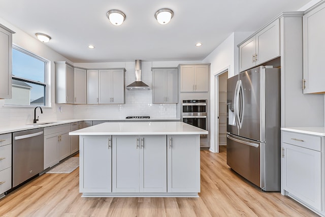 kitchen featuring gray cabinetry, a sink, appliances with stainless steel finishes, wall chimney range hood, and a center island