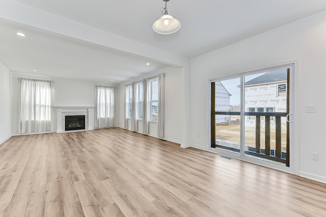 unfurnished living room featuring light wood finished floors, visible vents, baseboards, a glass covered fireplace, and recessed lighting