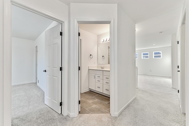 corridor featuring light carpet, baseboards, and a sink