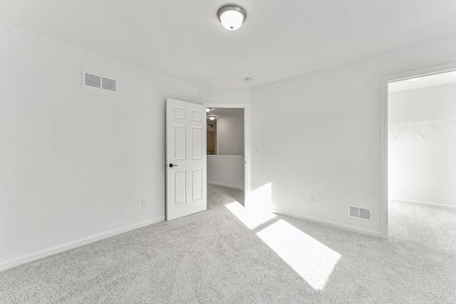 unfurnished bedroom featuring carpet floors, a walk in closet, visible vents, and baseboards