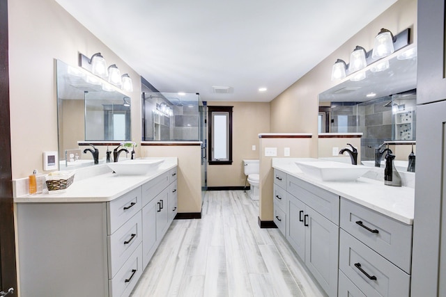 bathroom with wood finished floors, tiled shower, two vanities, and a sink