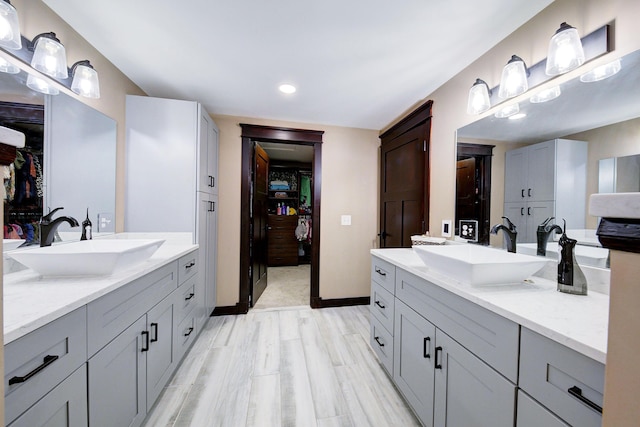 full bath with a walk in closet, two vanities, and a sink