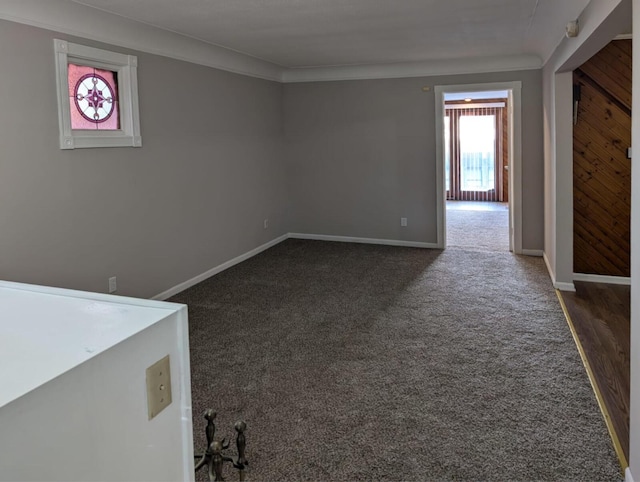 empty room with ornamental molding, dark carpet, and baseboards