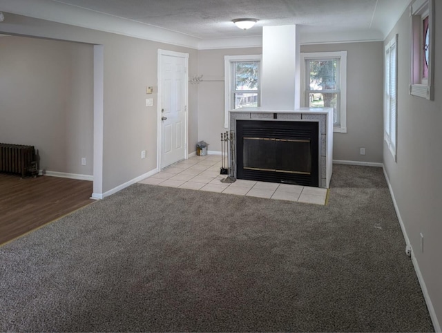 unfurnished living room featuring a healthy amount of sunlight, light carpet, a tiled fireplace, and radiator heating unit