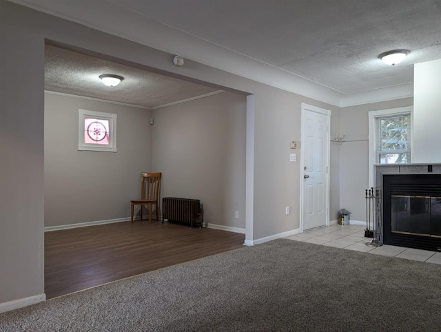 interior space featuring a textured ceiling, a tile fireplace, carpet floors, radiator, and crown molding