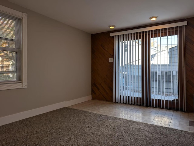 carpeted spare room with wood walls, tile patterned flooring, and baseboards