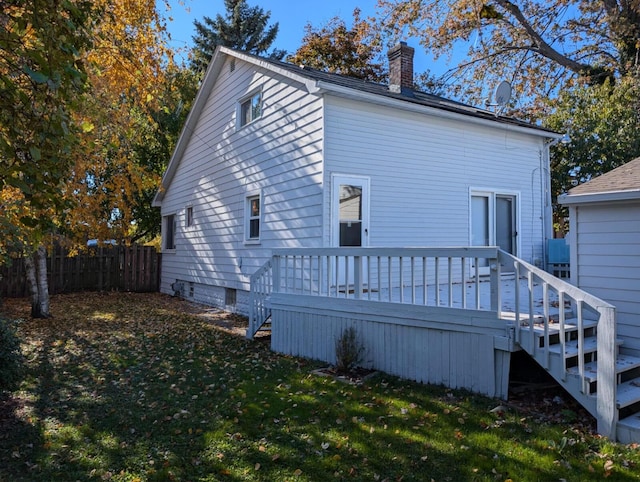 back of property featuring a chimney, fence, a deck, and a yard