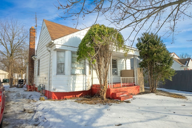 view of front of property featuring a shingled roof, covered porch, fence, and a chimney