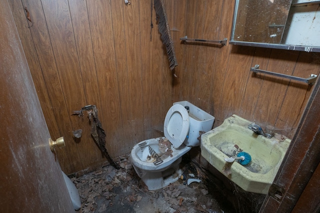 half bathroom featuring a sink, wood walls, and toilet