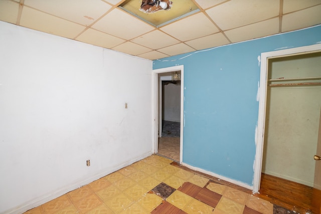 unfurnished bedroom with light floors, a closet, a paneled ceiling, and baseboards