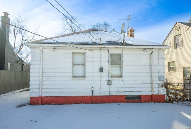 snow covered rear of property with a chimney and fence