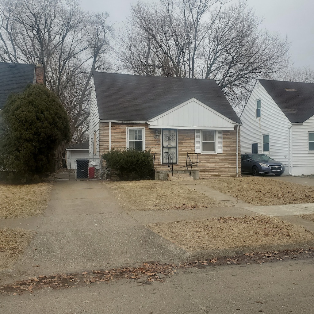 view of front facade with stone siding, roof with shingles, and driveway