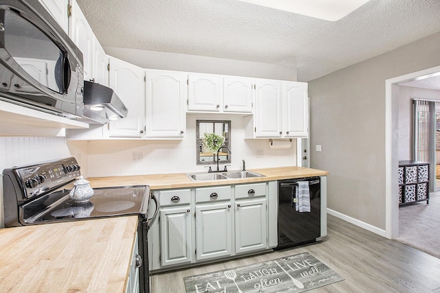 kitchen featuring butcher block counters, a sink, under cabinet range hood, and black appliances