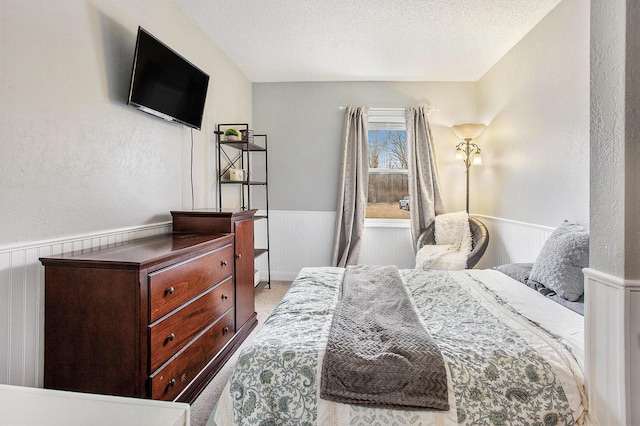 carpeted bedroom with wainscoting, a textured wall, and a textured ceiling